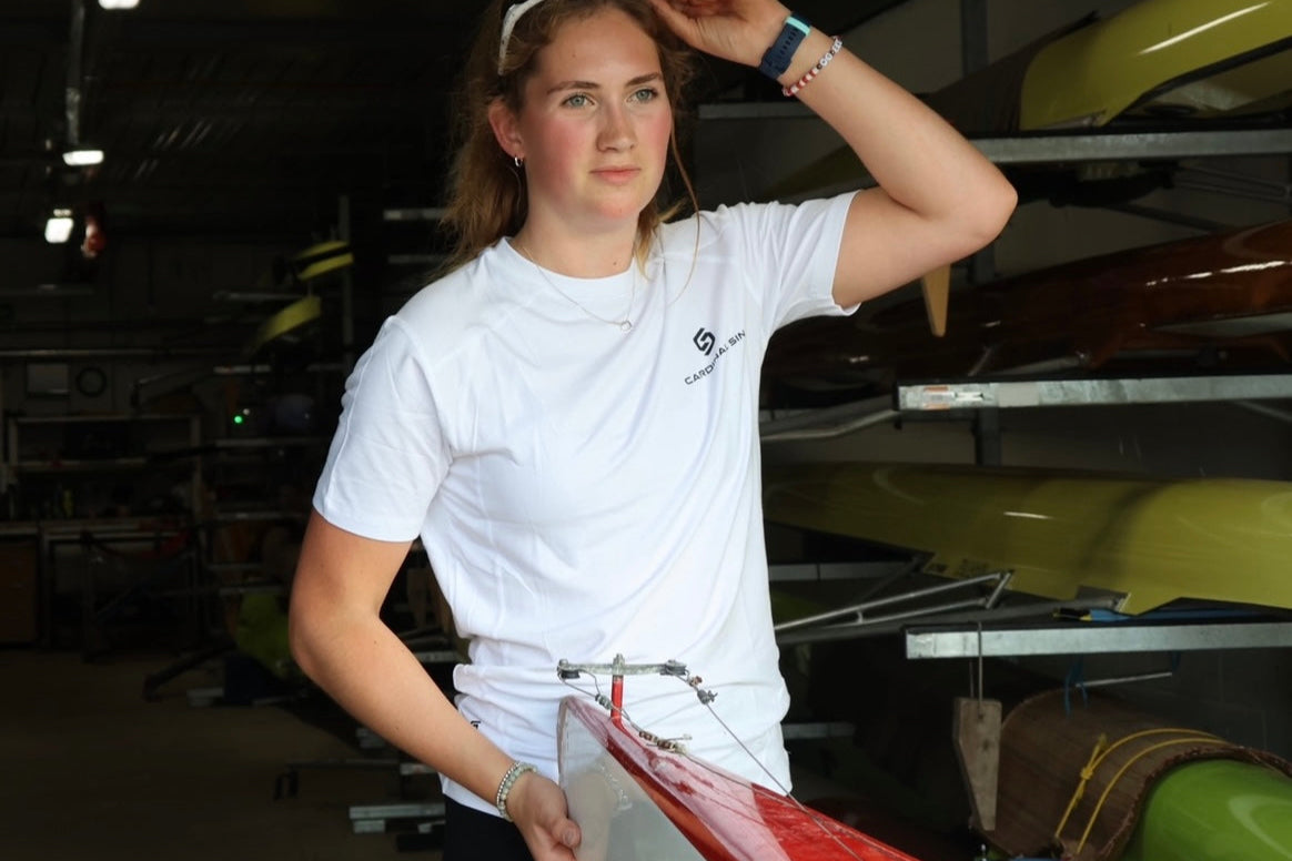 Person holding a red and white rowing boat in a storage area with kayaks.