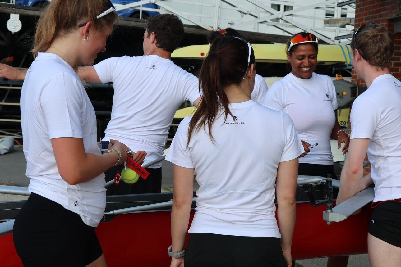 Group of people in white shirts and black shorts standing near a boat.