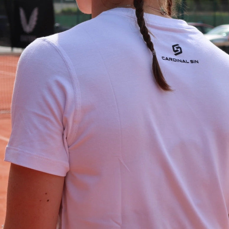 Person wearing a white shirt with a logo on a tennis court
